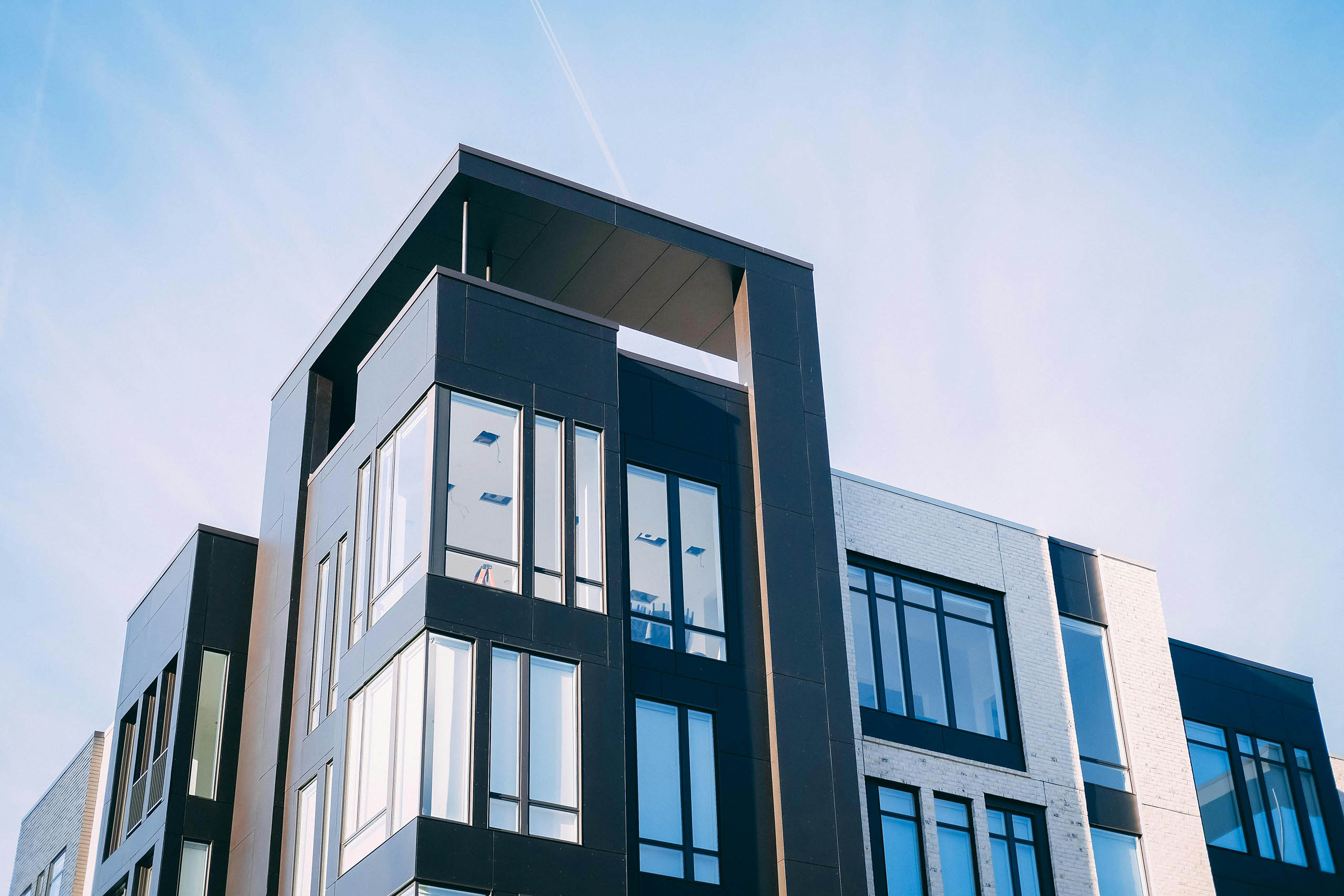 Modern apartment building with large glass windows and a mix of dark and light exteriors, supported by the Lancaster Housing Fund, offers affordable housing with clean lines, contemporary design, and beautiful views against a clear blue sky.