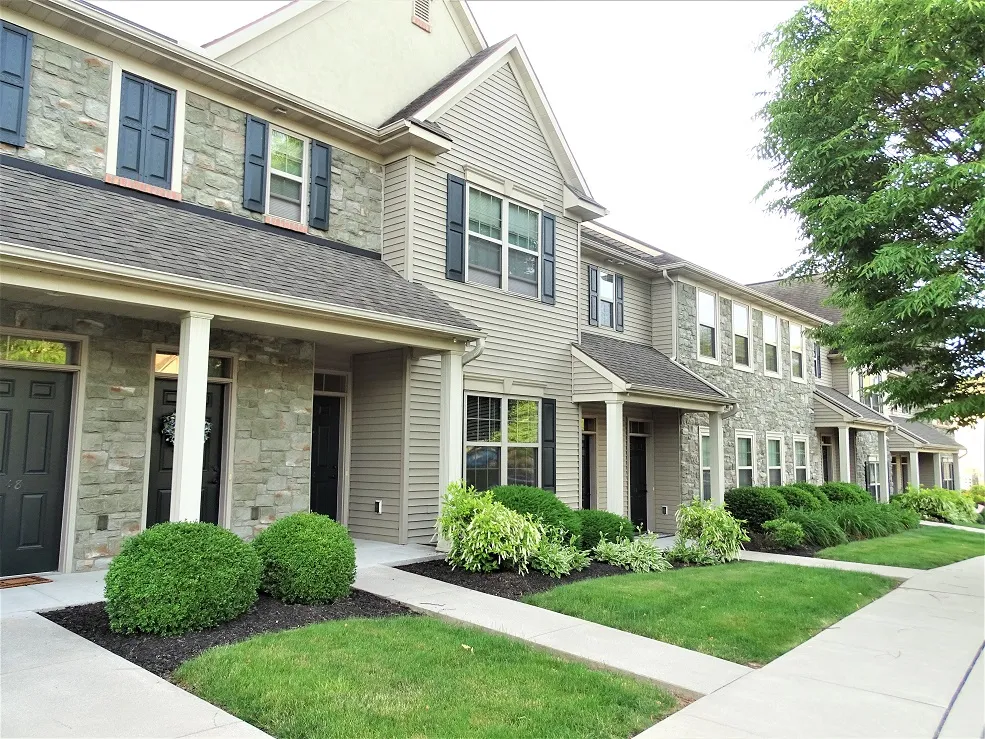 Row of modern two-story townhouses with stone and siding exteriors, black doors, front porches, neatly trimmed bushes, and green lawns along a clean concrete walkway—an inviting example of affordable housing supported by the Lancaster Housing Fund.
