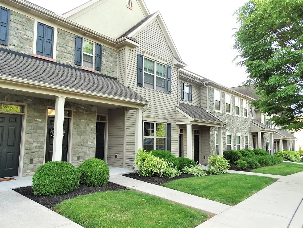 Row of modern two-story townhouses with stone and siding exteriors, black doors, front porches, neatly trimmed bushes, and green lawns along a clean concrete walkway—an inviting example of affordable housing supported by the Lancaster Housing Fund.