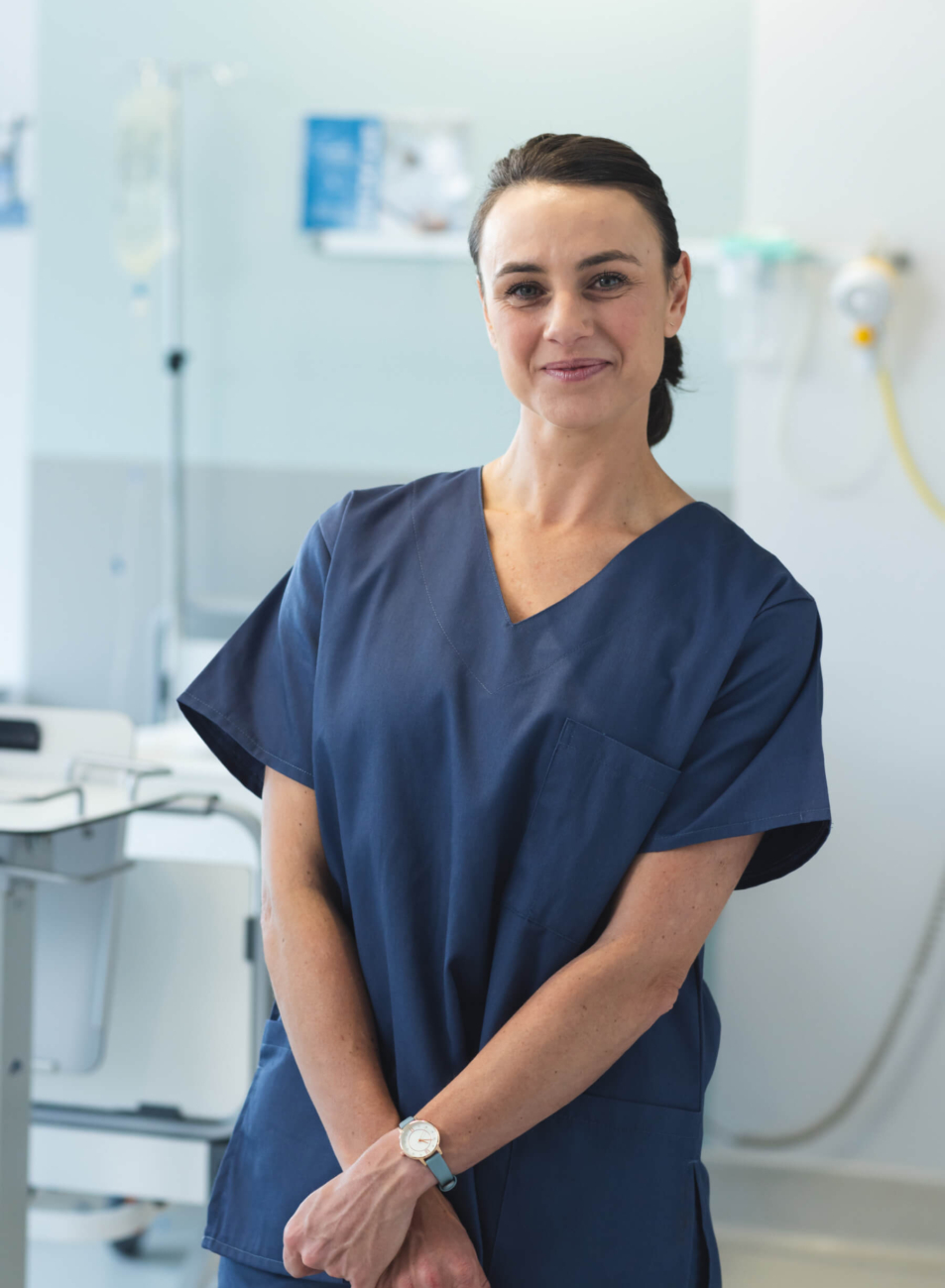 A smiling healthcare professional dressed in a navy scrub, standing confidently with arms crossed in a bright, modern medical environment.
